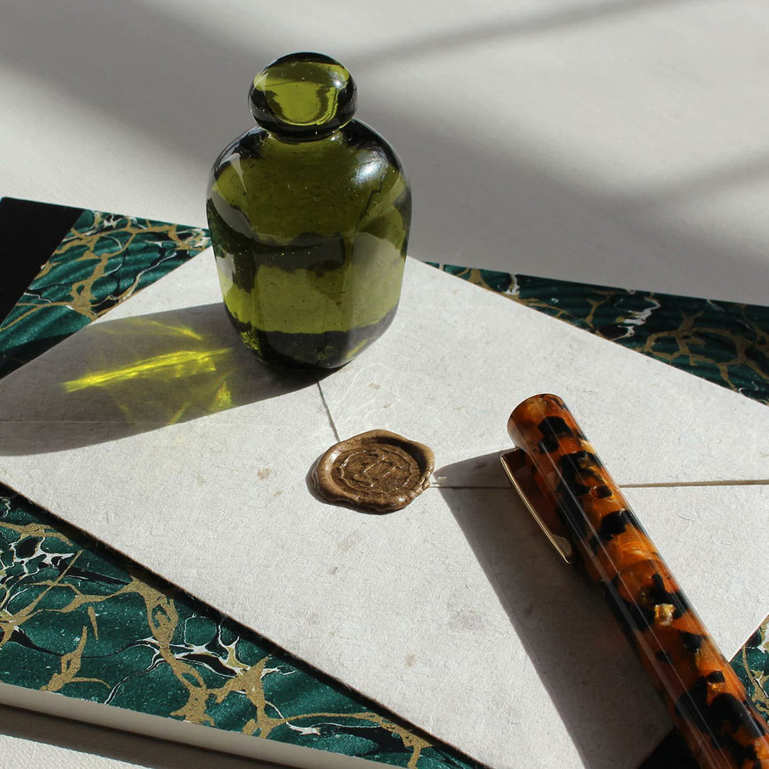 Discover the Attaché Recycled Glass Paperweight made from repurposed sake bottles in rich natural hues. A sustainable, handcrafted piece of Japanese glass art.