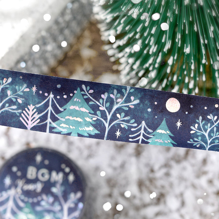 Strip of BGM Moonlit Forest washi tape in front of a frosted mini fir tree, foil details catching the light