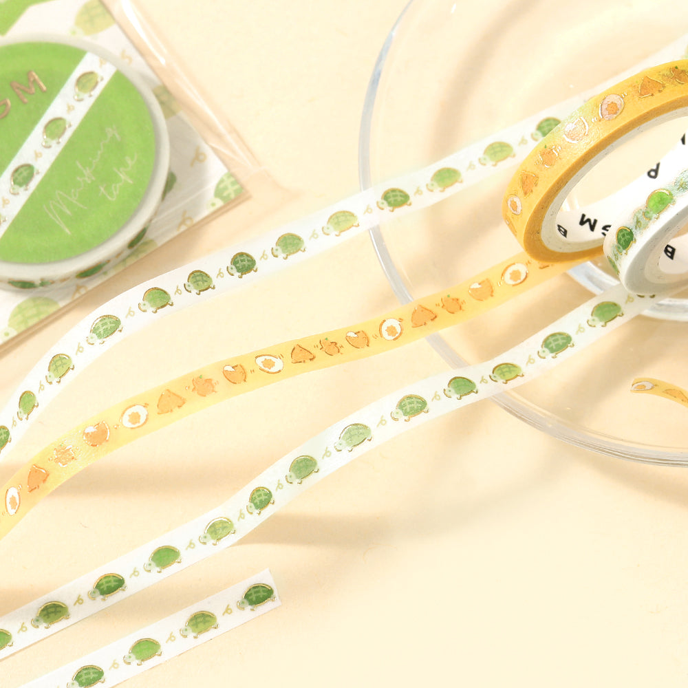 A slim roll of washi tape featuring a repeating design of playful yellow chicks running, accented with metallic foil highlights—perfect for planners, journaling, and decorative crafts.
