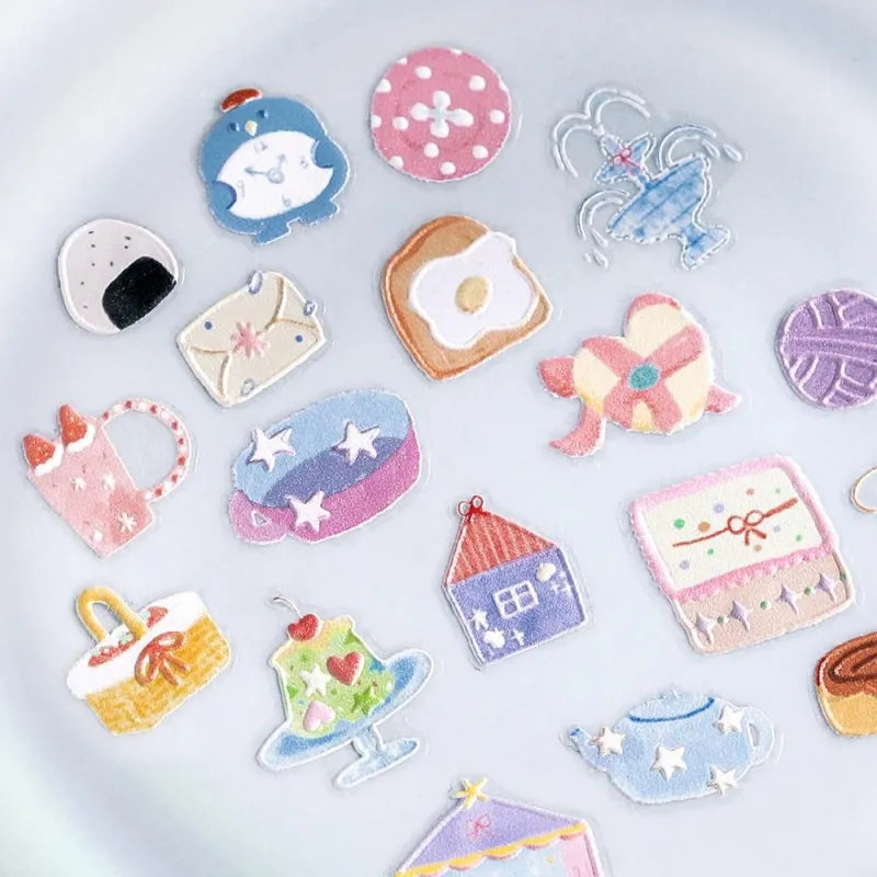 BGM Seat Seal – Colors of Life featuring a PET sticker sheet with pastel-toned icons of daily life: cameras, tea, yarn, sweets, and accessories, with a glossy embossed texture on a lavender background.