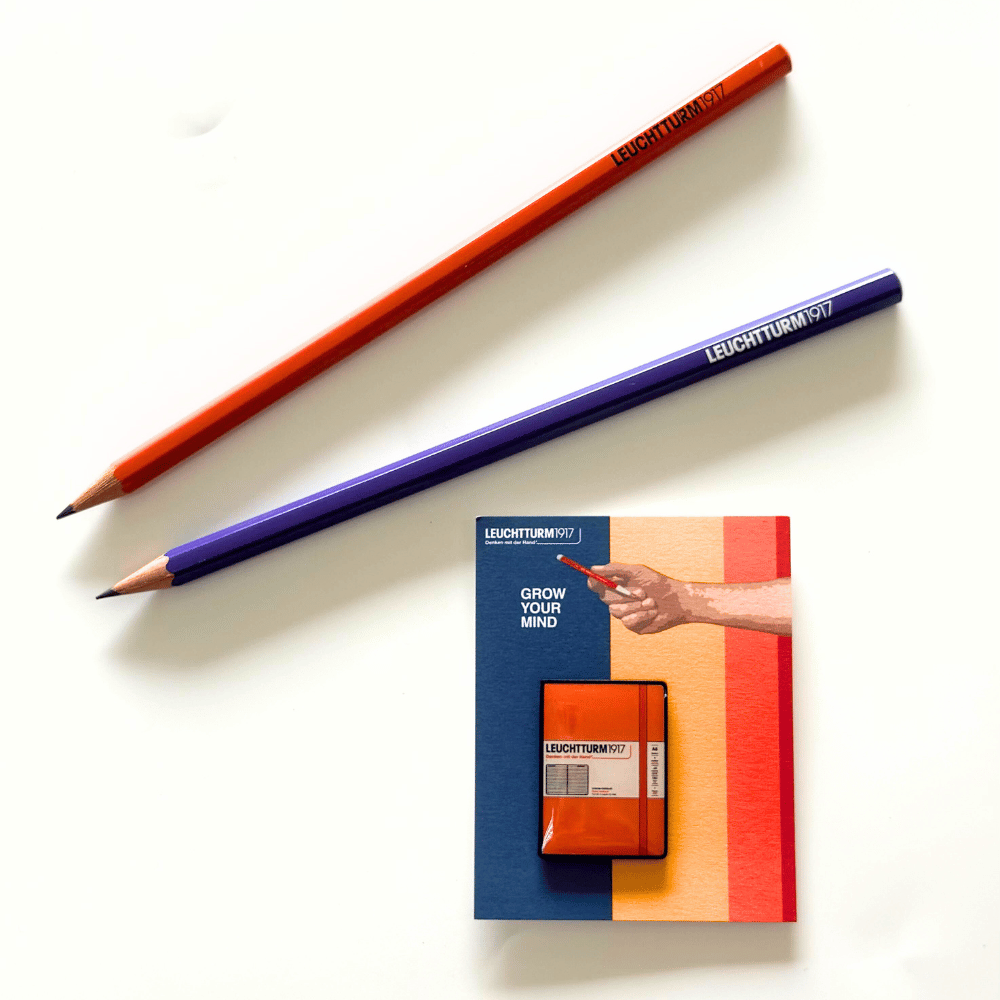 Leuchtturm1917 notebook pin in Pumpkin orange on its backing card, styled with pencils (not included)