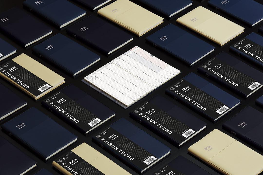 A professional A5 slim planner with a matte navy PVC cover and integrated pen holder. The refined monochrome design opens to neatly structured layouts—weekly vertical schedules, monthly blocks, project planning pages, and personal lists—all printed on smooth MIO PAPER for a premium, smudge-resistant writing experience.