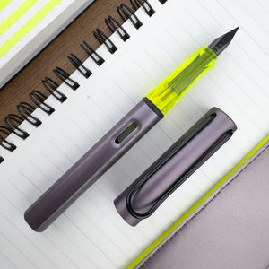 LAMY AL-star fountain pen in metallic aubergine with a translucent neon yellow grip, black steel nib, and metal clip. Includes a blue ink cartridge.