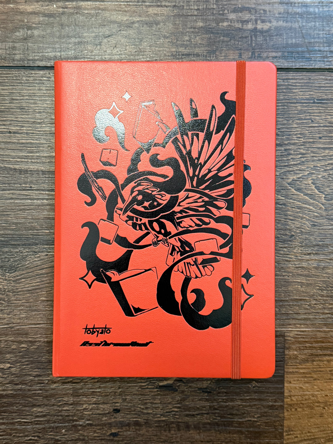 Leuchtturm1917 Tobyato Edition A5 Medium Notebook in fox red with dotted pages, featuring a cover design of a raven with books and typewriter keys, symbolizing knowledge and resilience.