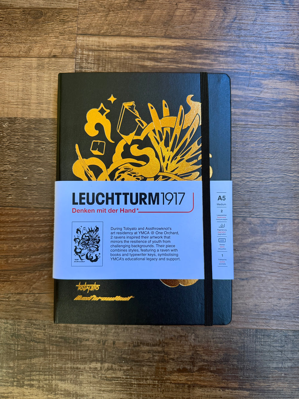 Leuchtturm1917 Tobyato Edition A5 Medium Notebook in black with ruled pages, featuring a cover design of a raven surrounded by books and typewriter keys, symbolizing creativity and knowledge.