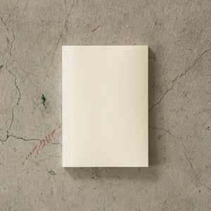 A5 MD Notebook Diary 2026 with a minimalist cream-toned glassine paper cover, thread-stitched binding, and a white bookmark string. The open spread displays a block-style monthly calendar on one side and lined memo pages on the other, printed on smooth MD PAPER designed for a premium writing experience.