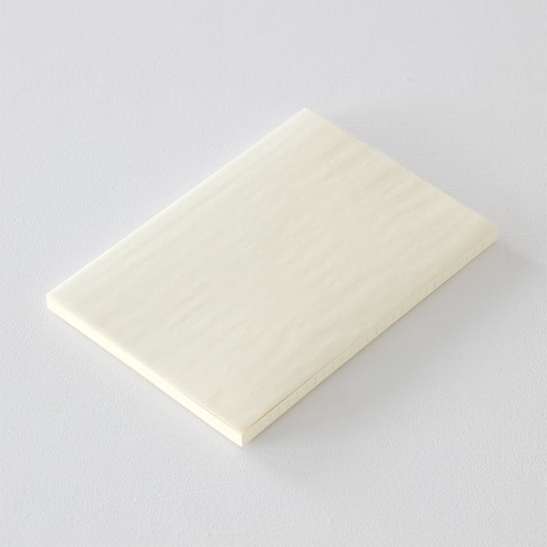 Load image into Gallery viewer, A5 MD Notebook Diary 2026 with a minimalist cream-toned glassine paper cover, thread-stitched binding, and a white bookmark string. The open spread displays a block-style monthly calendar on one side and lined memo pages on the other, printed on smooth MD PAPER designed for a premium writing experience.
