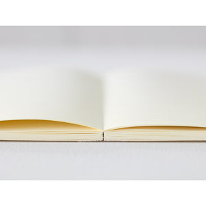 A5 MD Notebook Diary 2026 with a minimalist cream-toned glassine paper cover, thread-stitched binding, and a white bookmark string. The open spread displays a block-style monthly calendar on one side and lined memo pages on the other, printed on smooth MD PAPER designed for a premium writing experience.