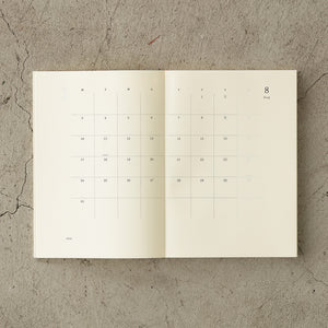 MD Notebook Diary (A5) Thin 2026 – A slim, thread-bound diary with a minimalist cream cover and glassine paper wrap, featuring monthly schedule pages, 5mm grid memo pages, and a bookmark string. Compact and lightweight, designed for portability and everyday use.