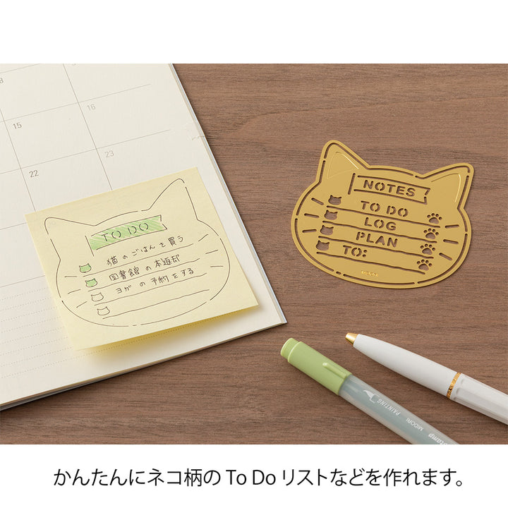 A slim brass stencil with cut-out cat faces, paw prints, and checklist boxes, designed for decorating planners, notebooks, and memos.